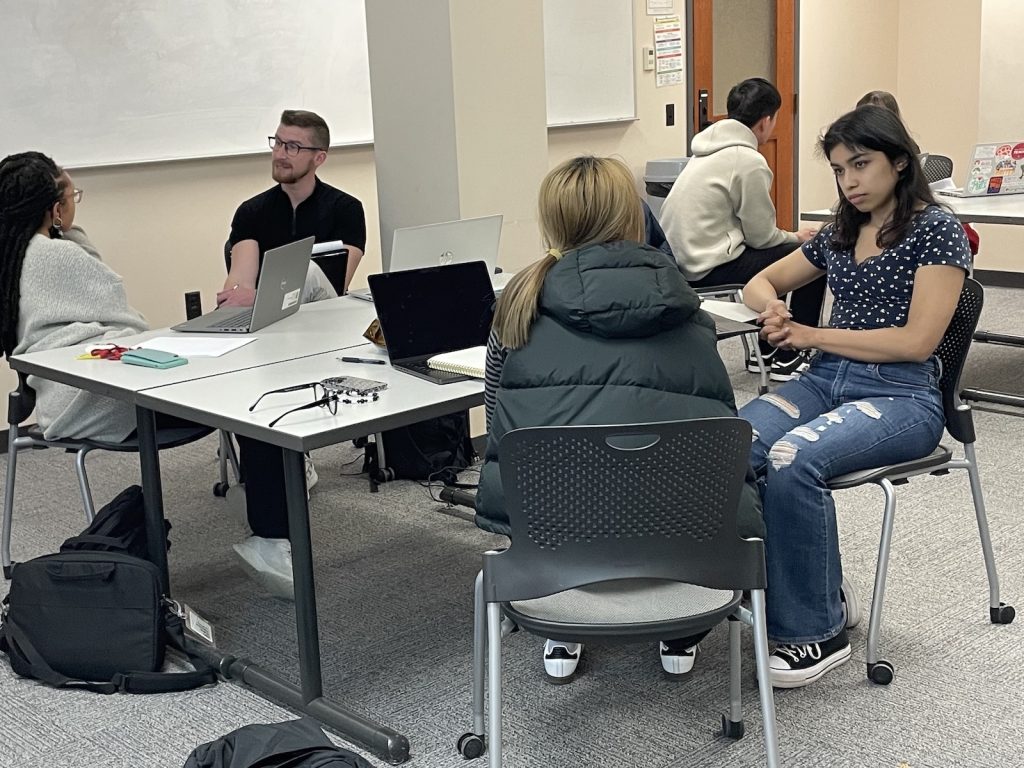 Six students, sitting in three groups of two, in ELPA 824 are sitting at tables in a classroom in the School of Education Building and discussing course material.