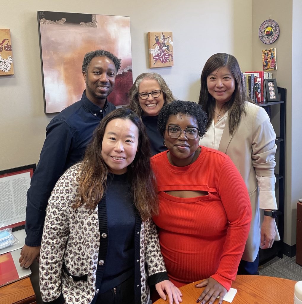 A group picture of Higher Education professors smiling at the camera in an office. From left to right, the picture features (front row) Dr. Jing Yu, Dr. Aireale Rodgers, (back row) Dr. Brian Burt, Dr. Rachelle Winkle-Wagner, and Dr. Xueli Wang