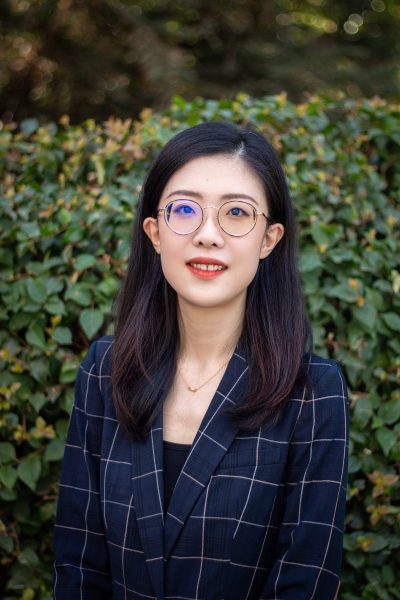 A headshot of Dr. Xiwei Zhu, who is smiling in front of a green leafy wall.