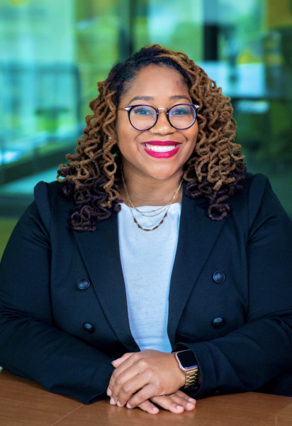 A headshot of Dr. LaShawn Faith Washington, who is sitting with her arms crossed and smiling in front of a School of Education Building glass wall.