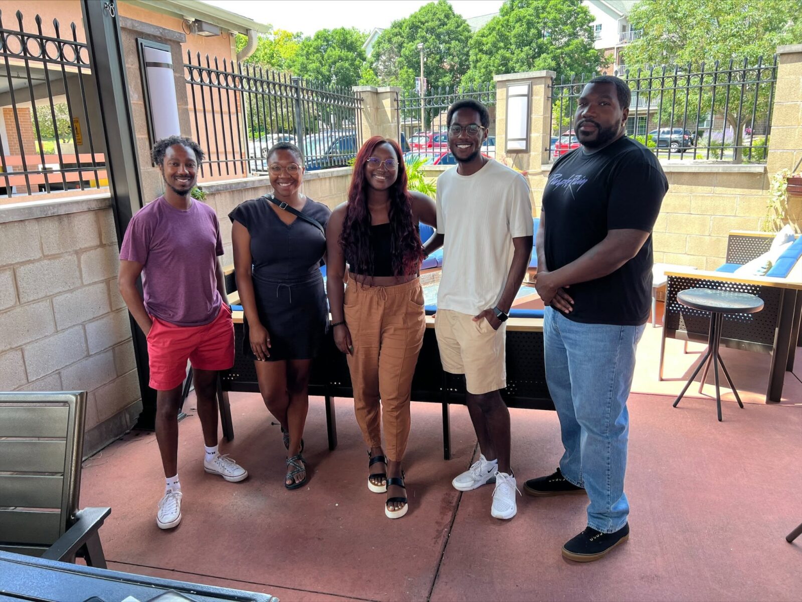 Dr. Brian A. Burt stands outside at a table in the shade with a group. From Left to right: Dr. Burt, (now Dr.) Tiaira Porter-Beall, Dr. Dajanae Palmer, Devin Henry, and (now Dr.) Blayne Stone, Jr.).