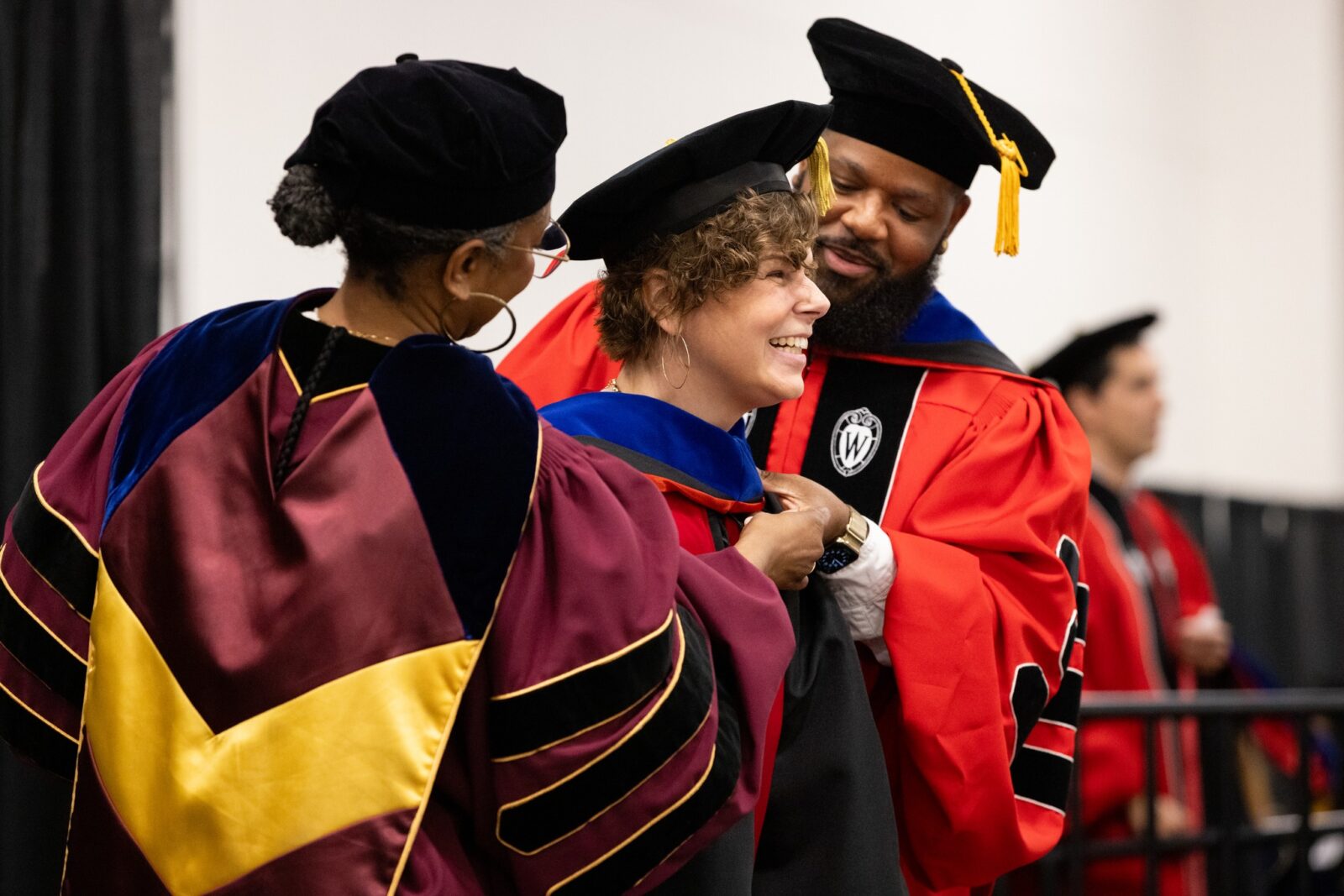 PhD Student Maggy Olson has a huge smile while being hooded at graduation by Dr. Kevin Henry and Dean Marcelle Haddix.